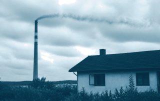 Chaminé industrial com fumaça passando sobre casa com janela aberta