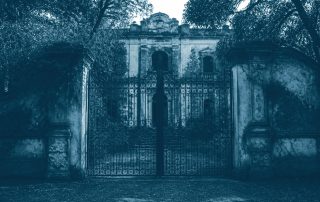 Portão de ferro fechado diante de prédio colonial em ruínas