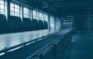 Chão de fábrica vazio com esteira parada sob luz industrial