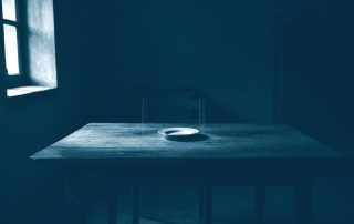 Mesa de jantar vazia com prato único sob luz fraca