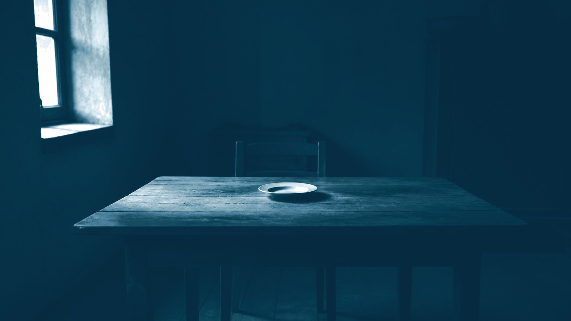 Mesa de jantar vazia com prato único sob luz fraca