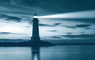 Farol aceso contra o céu ao entardecer, mar calmo